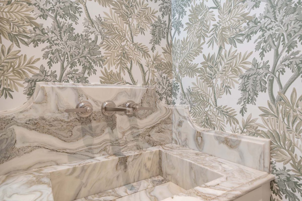 Lavabo de mármol veteado sobre papel pintado de motivo vegetal